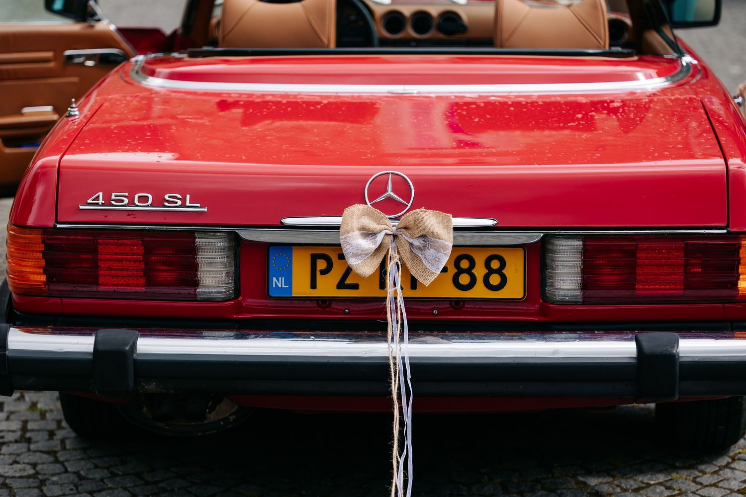 Red Mercedes-Benz 450SL convertible with a decorative bow on the trunk and Dutch license plate PZ-88.