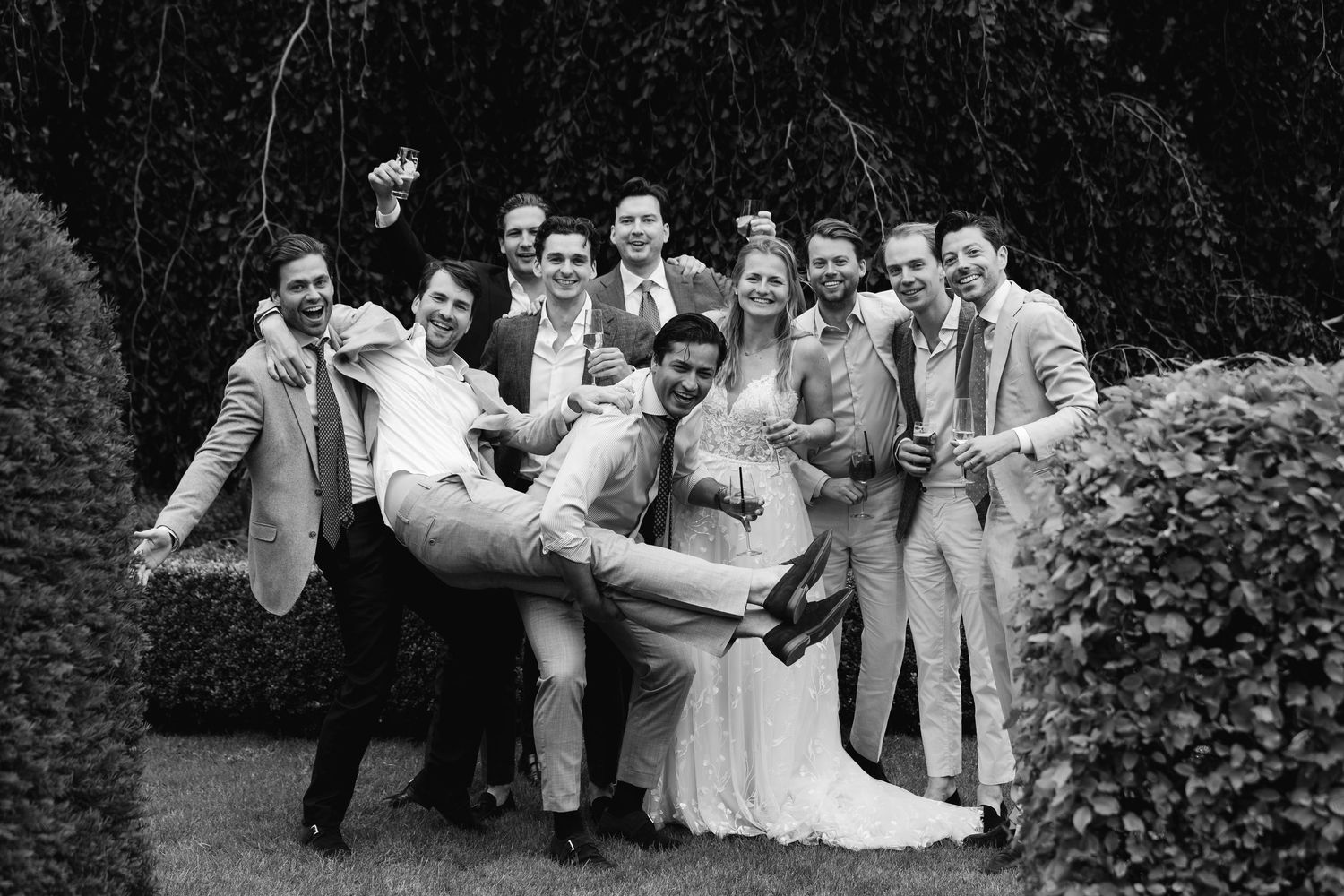 Wedding party posing playfully in black and white photo with groom being lifted.