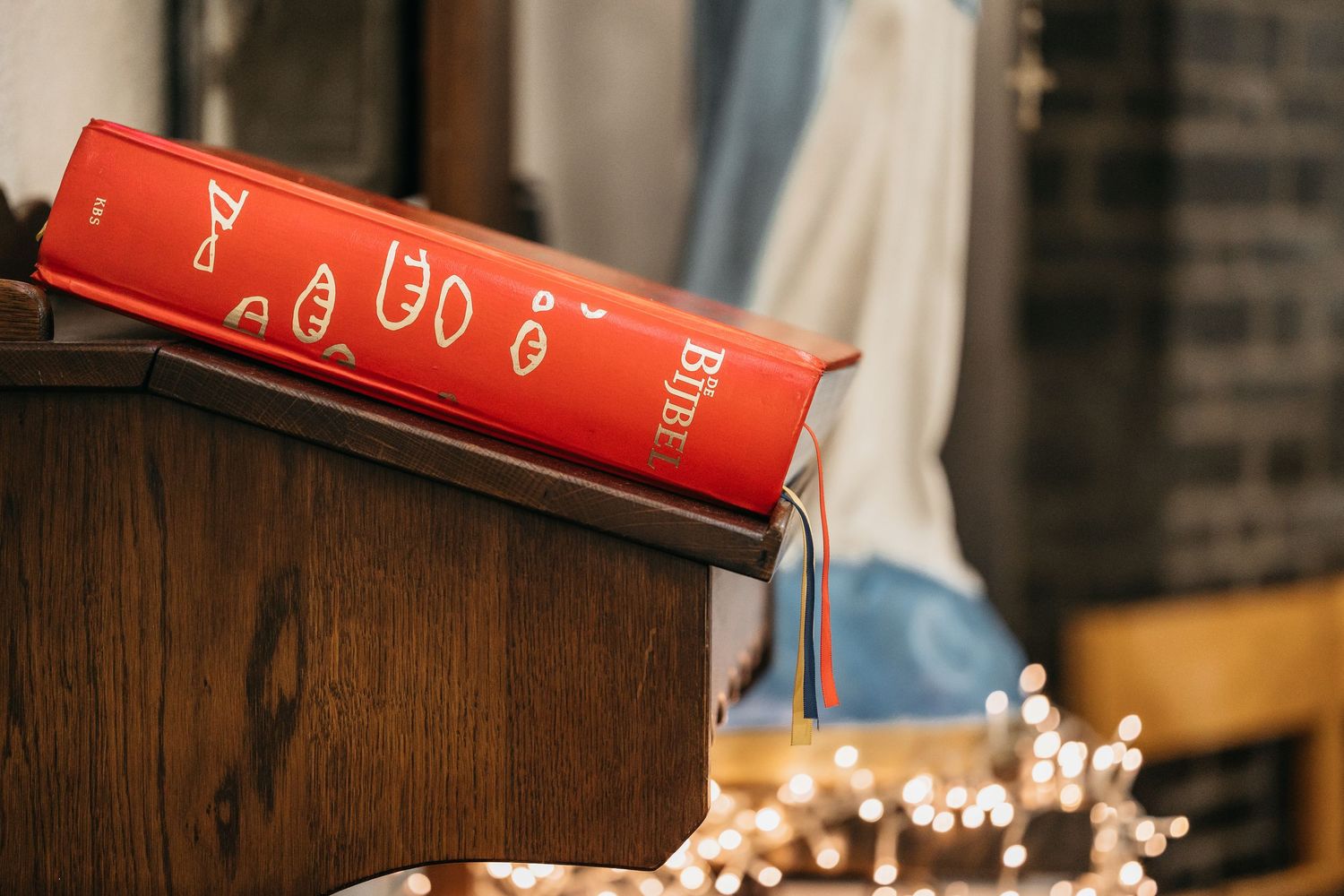 Red Holy Bible resting on wooden church pulpit with bokeh lights in background.