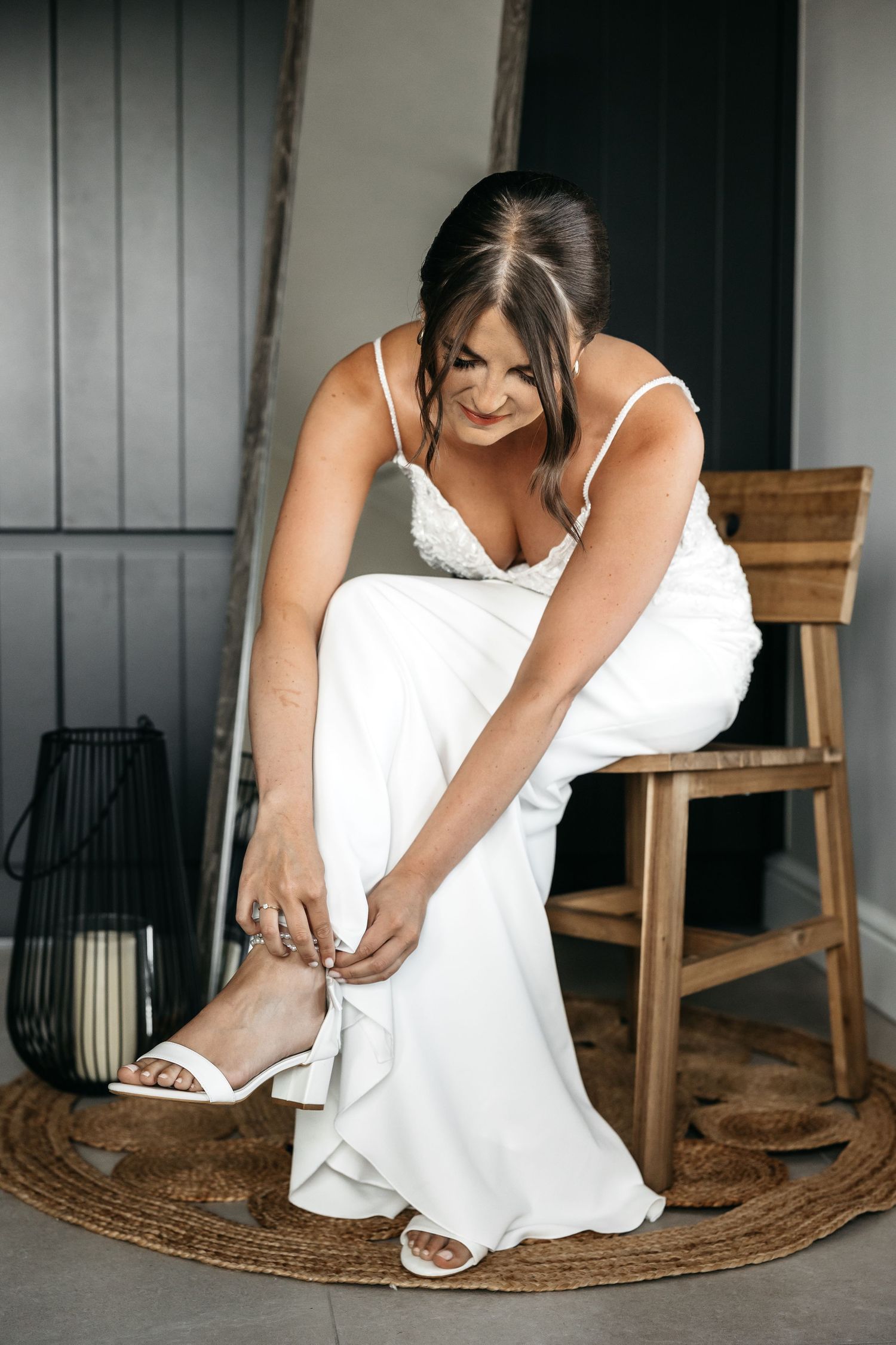 Bride in white lace wedding dress buckling her white block heel sandals while seated.