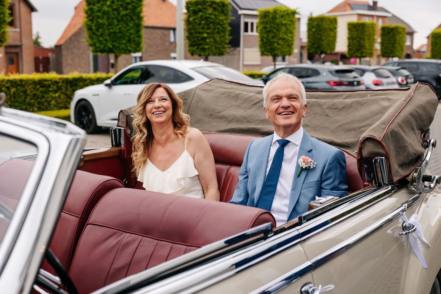 Smiling bride and groom ride in a classic vintage convertible car on their wedding day.