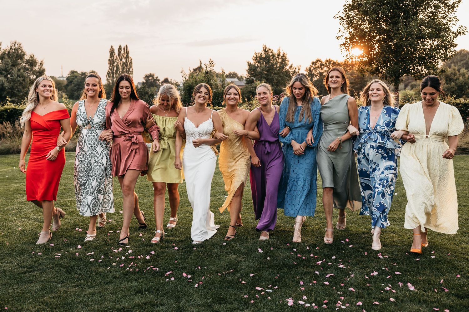 Bride and female guests laughing and walking together in colorful dresses at golden hour.
