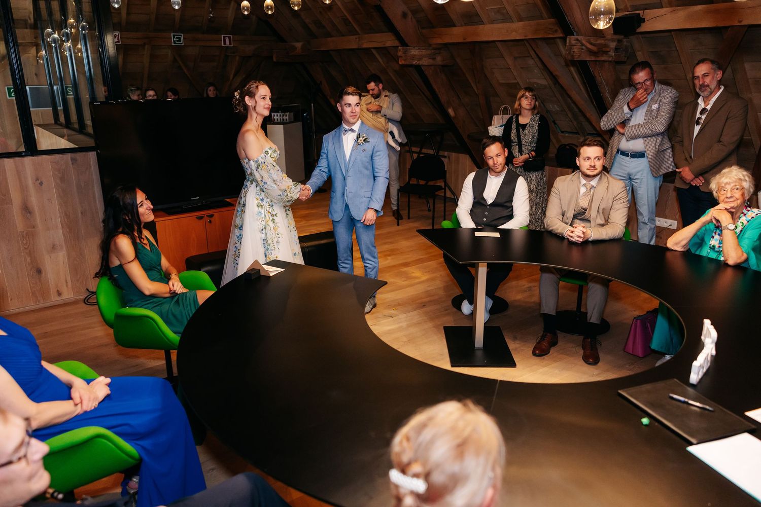 Newlywed couple stands hand in hand before seated wedding guests in rustic barn venue.