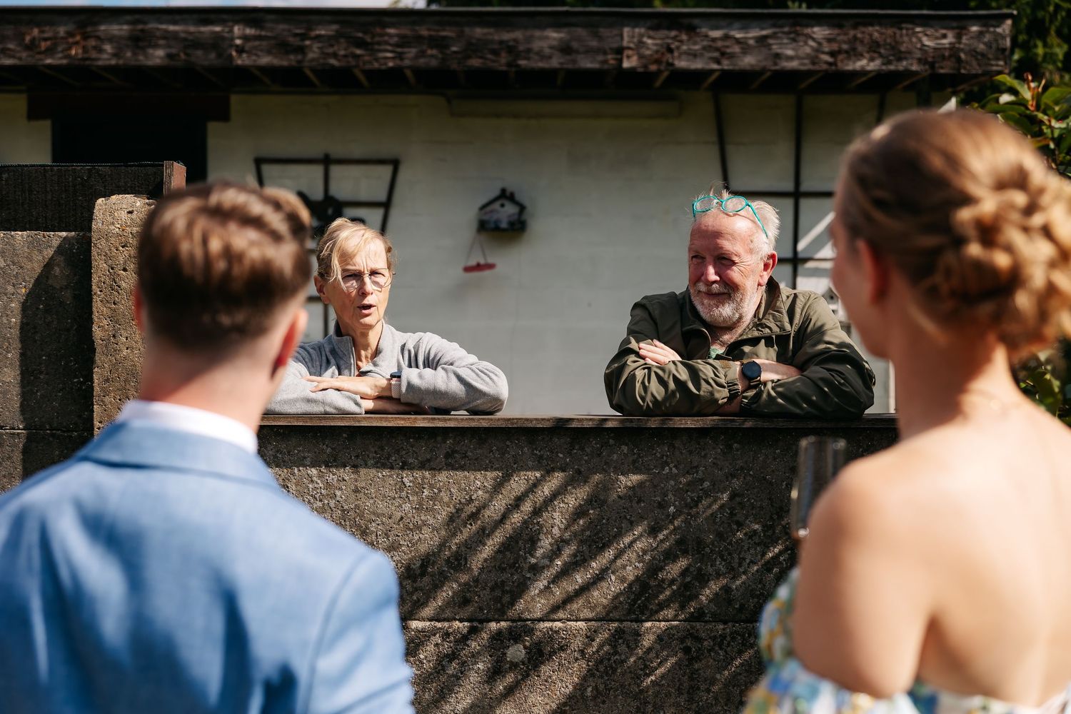 Bride and groom speaking with two older men leaning on a stone wall.