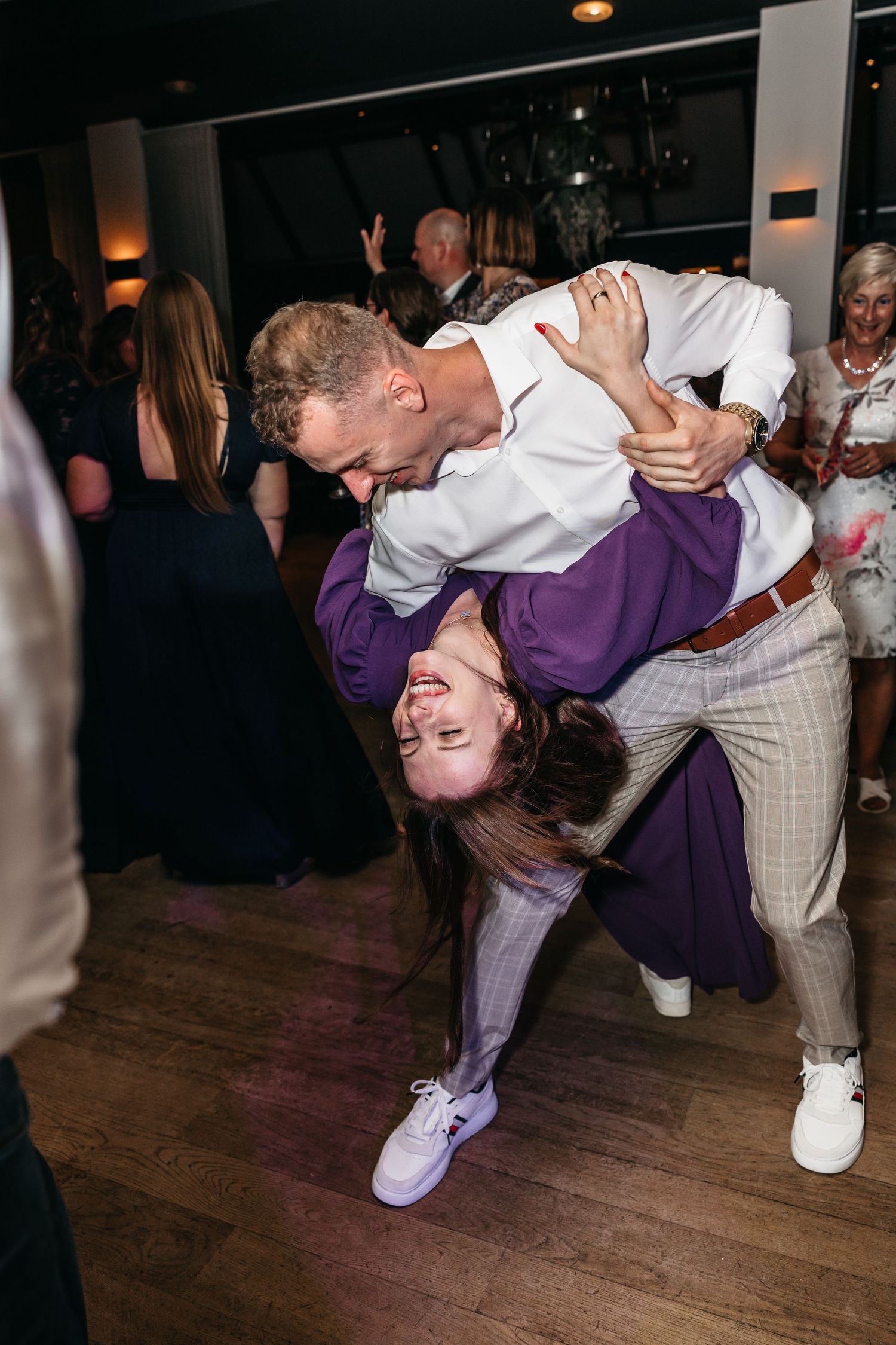 Wedding guest in purple dress gets dramatically dipped by a partner on the lively wedding reception dance floor.