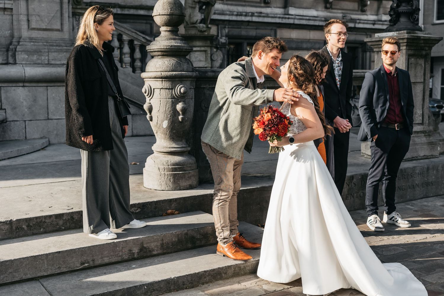 Groom kissing bride in white dress on steps while wedding guests watch at outdoor ceremony.
