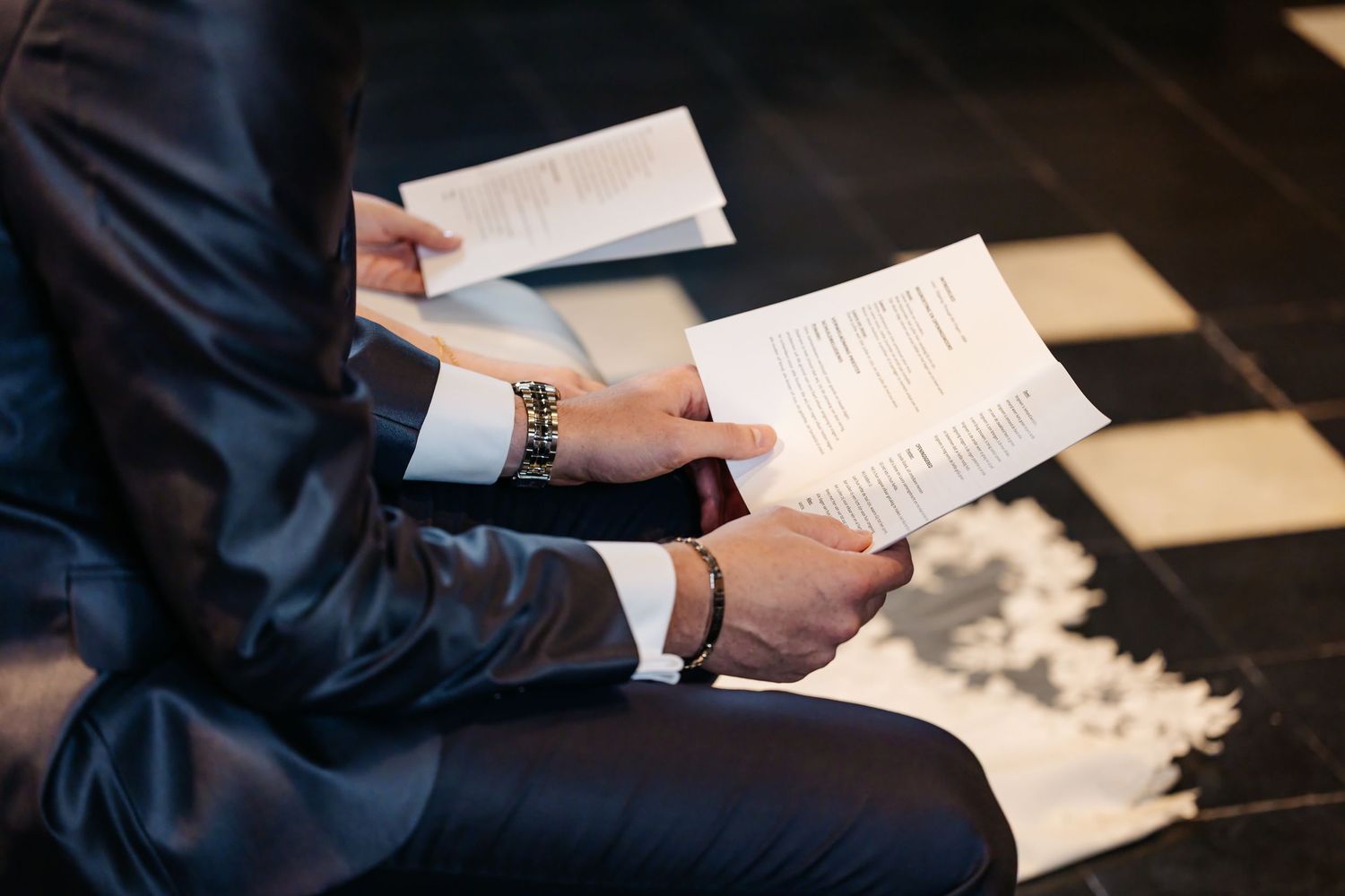 Groom in dark suit reviewing wedding ceremony programs while seated.