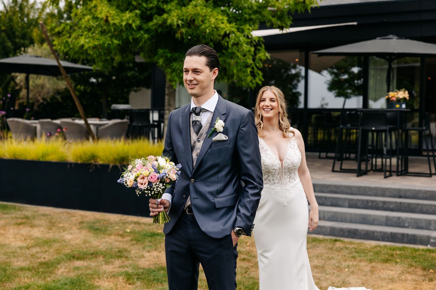 Bride and groom walking hand in hand outdoors, groom holding colorful wedding bouquet.