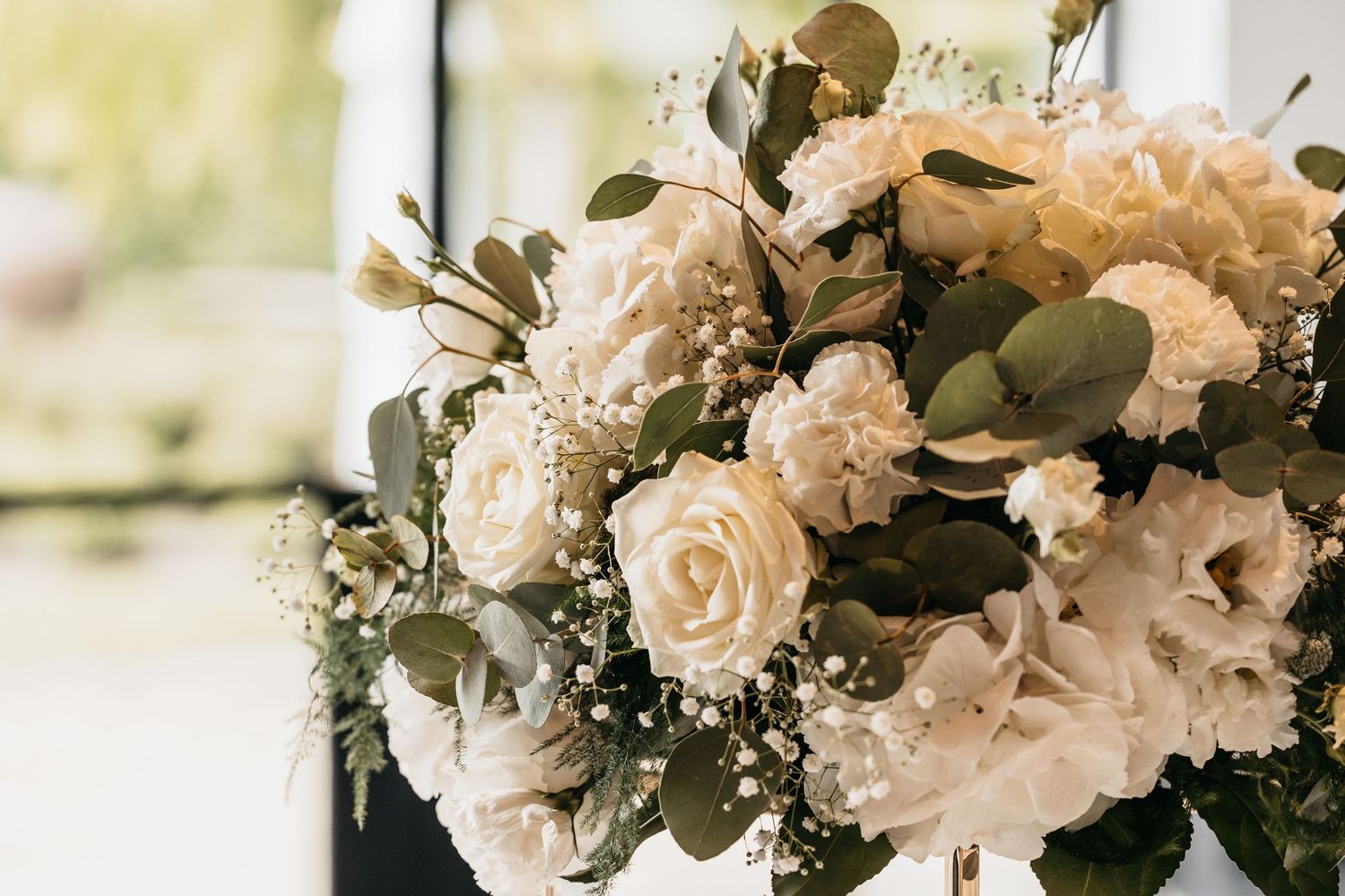 Beautiful wedding bouquet featuring white roses, hydrangeas, eucalyptus, and baby's breath in soft natural light.