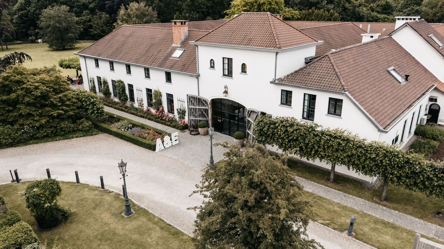 Aerial view of elegant white wedding venue with terracotta roof and manicured grounds.
