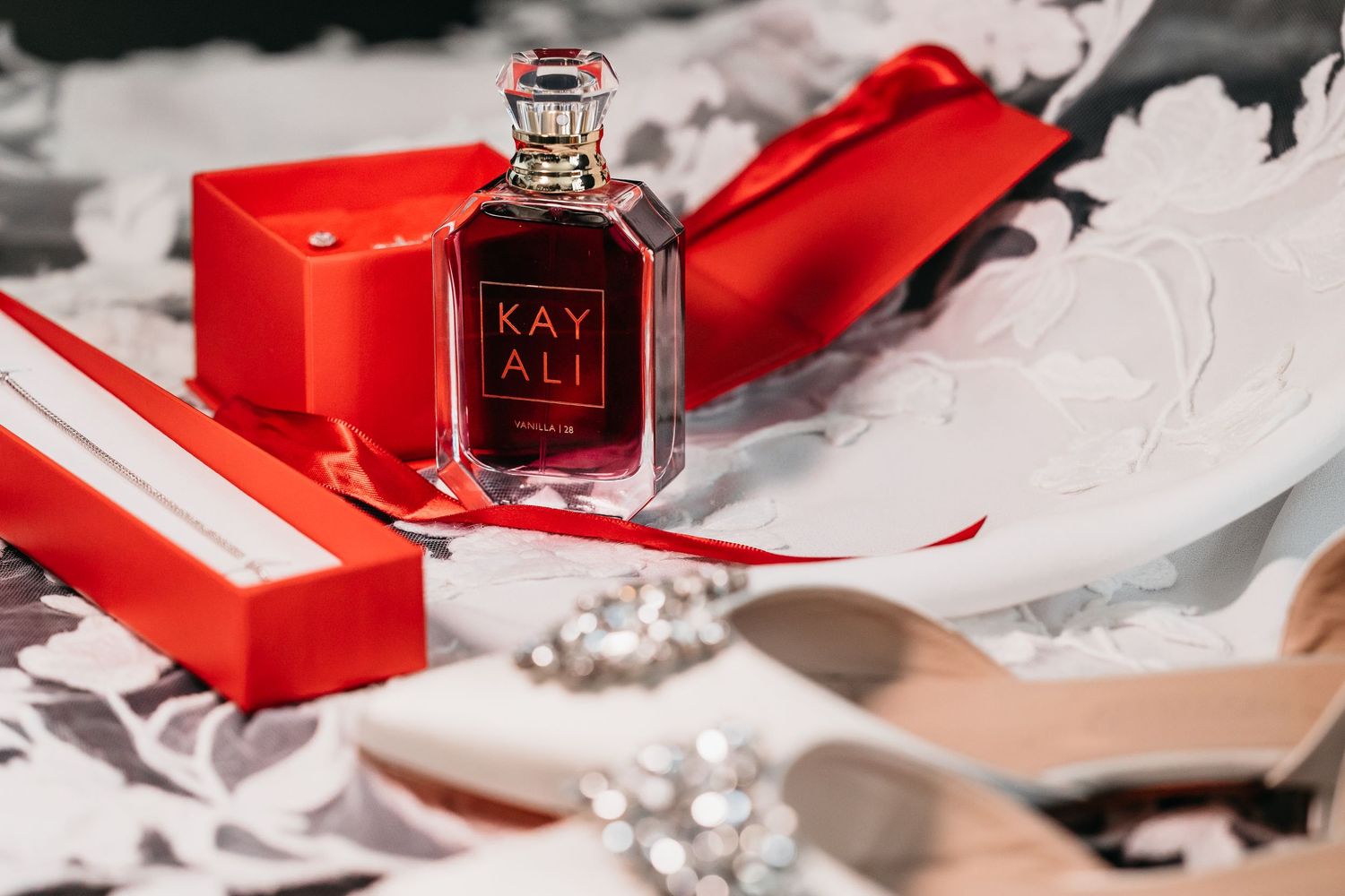 Kayali perfume bottle in red gift box with white lace fabric and crystal shoe detail.