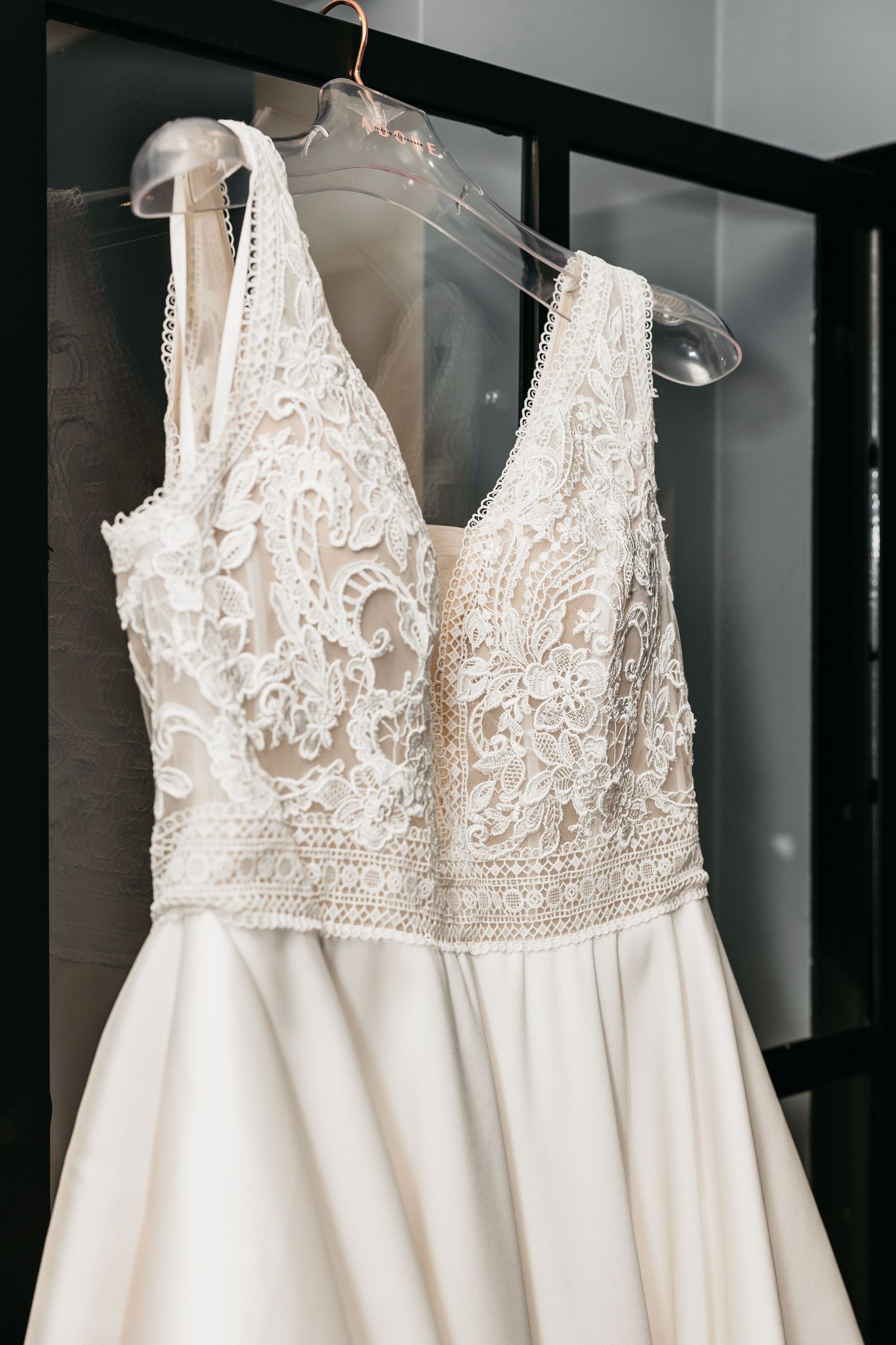 Close-up of a white lace V-neck wedding dress bodice with floral embroidery on a hanger.