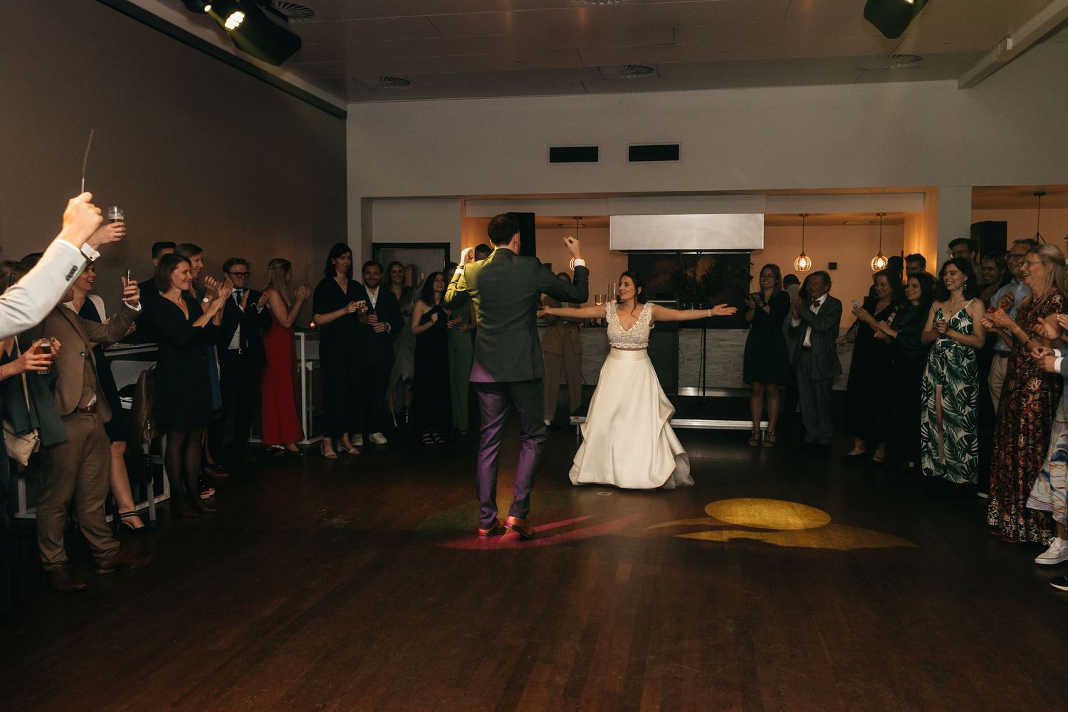 Bride and groom celebrate on dance floor surrounded by cheering wedding guests.