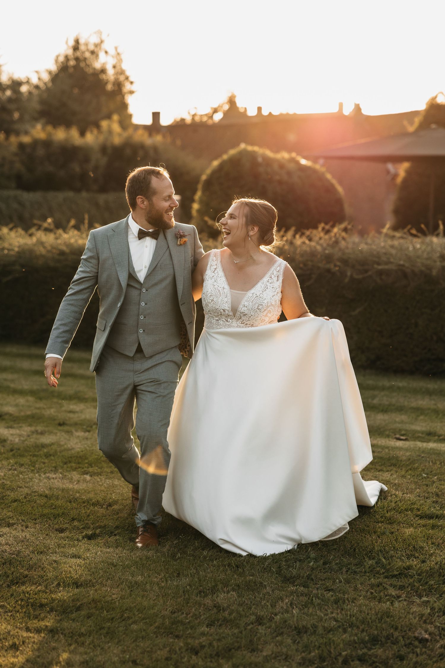 Laughing bride and groom walking through garden at golden hour sunset on their wedding day.