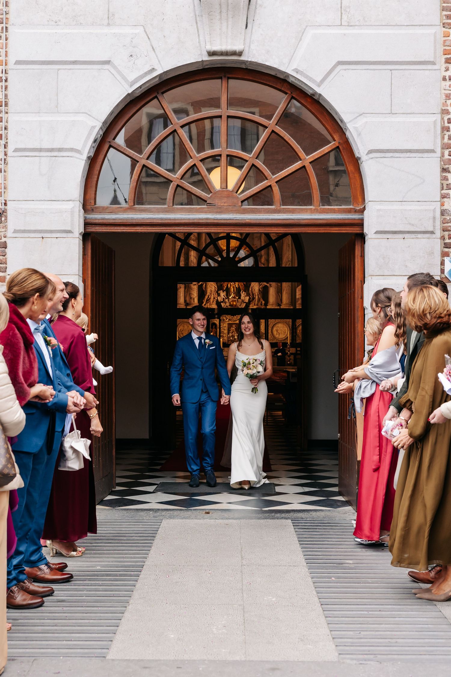 Newlyweds exit church doors as guests line up to celebrate their wedding ceremony.