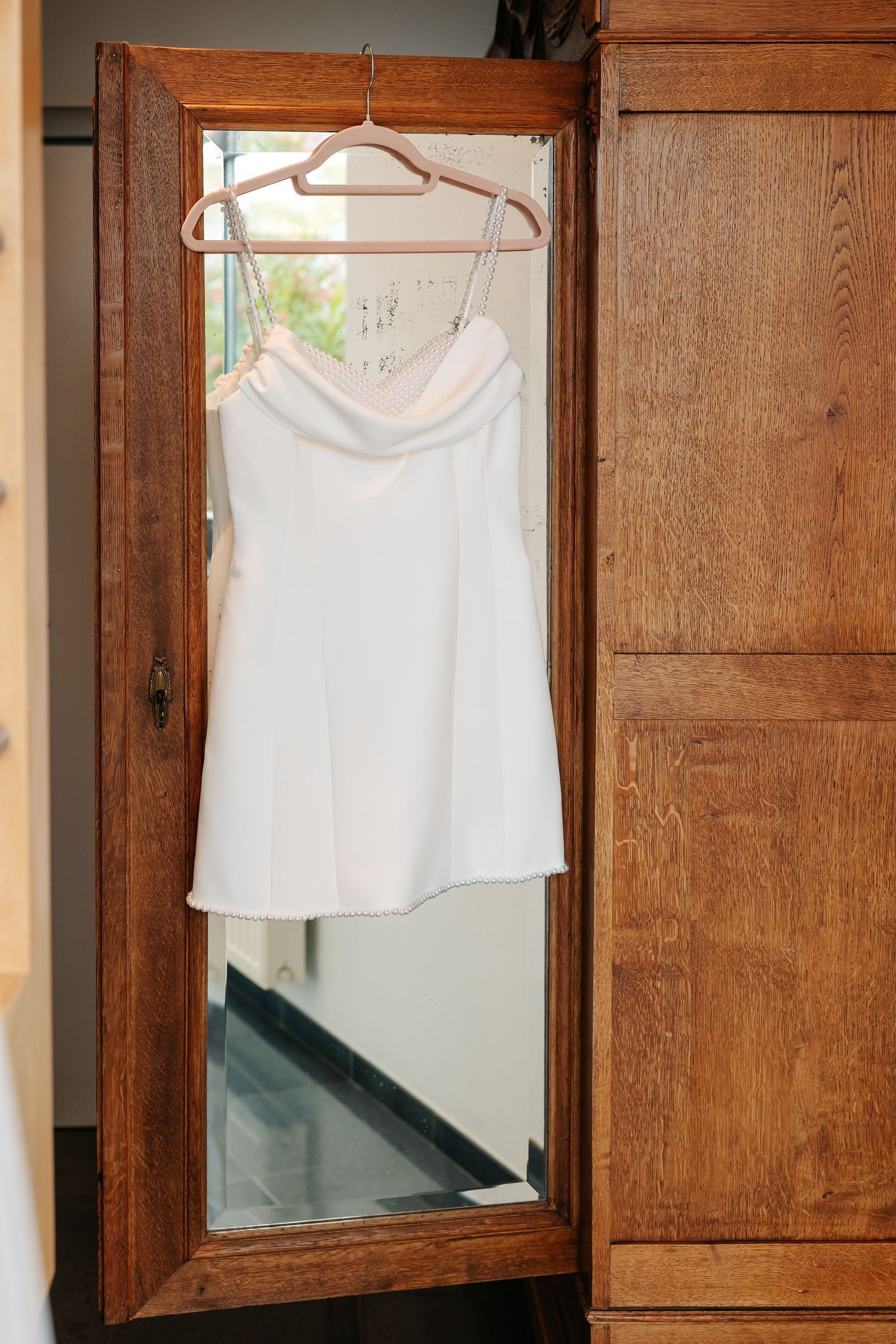 White bridal mini dress reflected in an antique wooden mirror wardrobe.