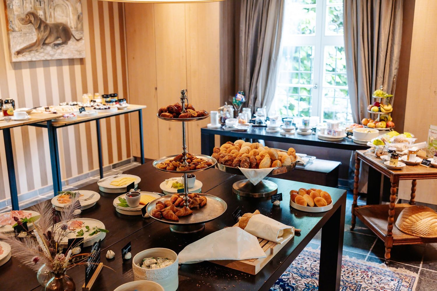 Elegant breakfast buffet spread with croissants, pastries, and fresh dishes on dark wood tables in a stylish dining room.