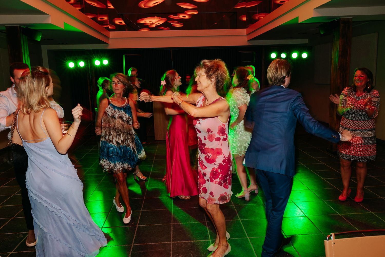 Guests dancing energetically on a colorful lit dance floor during a lively wedding reception party.
