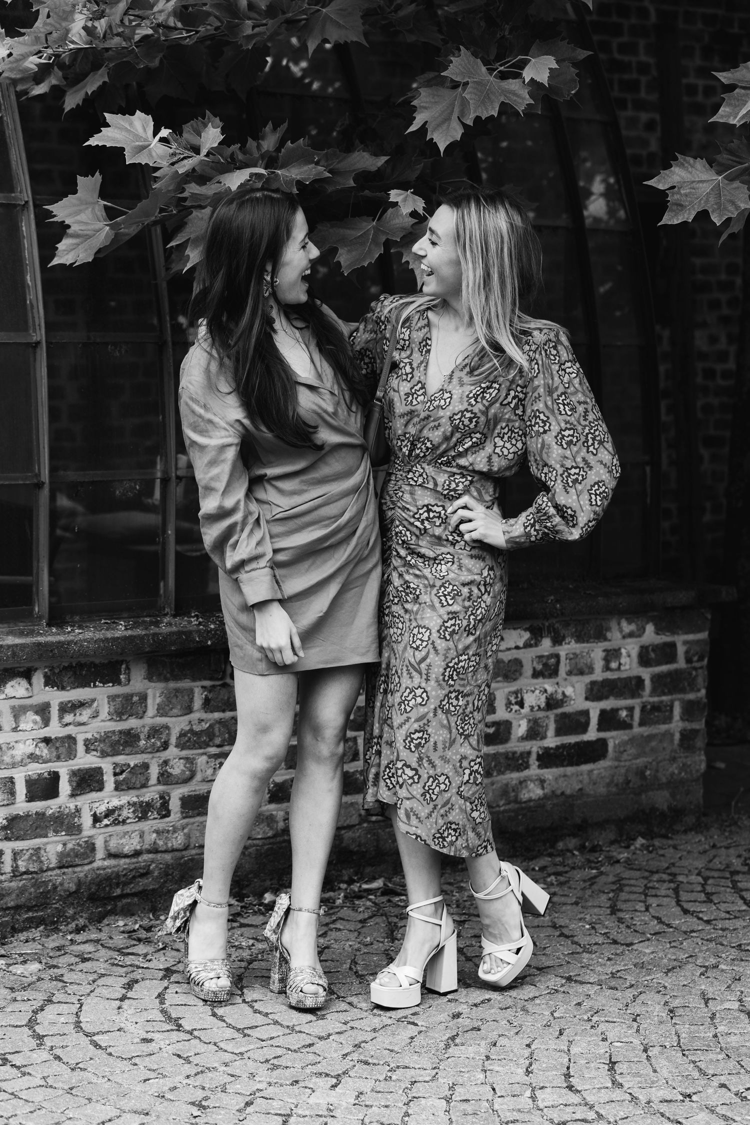 Two elegant women in stylish dresses laughing together in black and white photo.