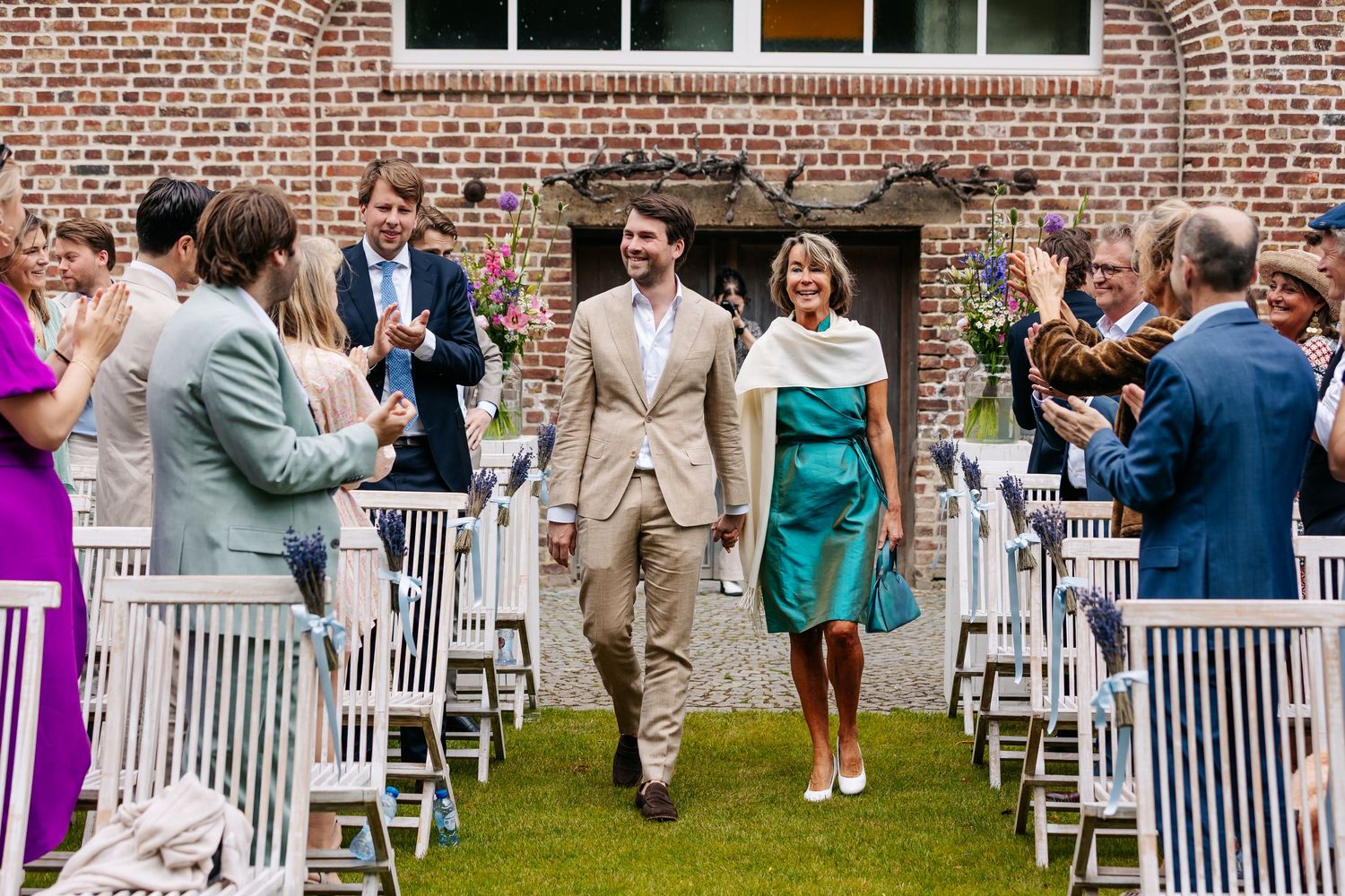 Newlyweds walk joyfully down the aisle as guests applaud at an outdoor wedding ceremony.