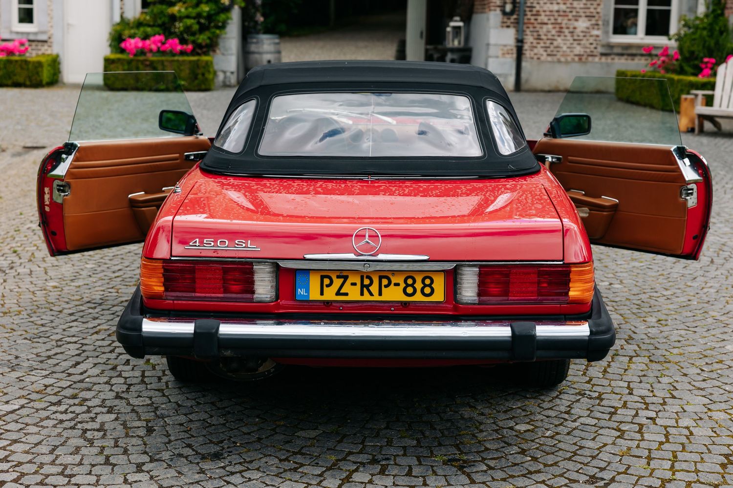 Red Mercedes-Benz 450SL classic convertible with open doors, Dutch license plate PZ-RP-88, parked on cobblestone.