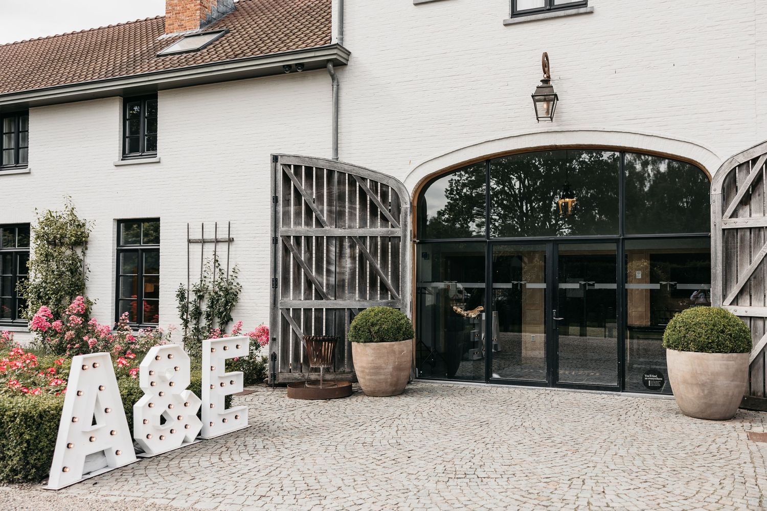 White wedding venue exterior with large A&E marquee letters on cobblestone courtyard.