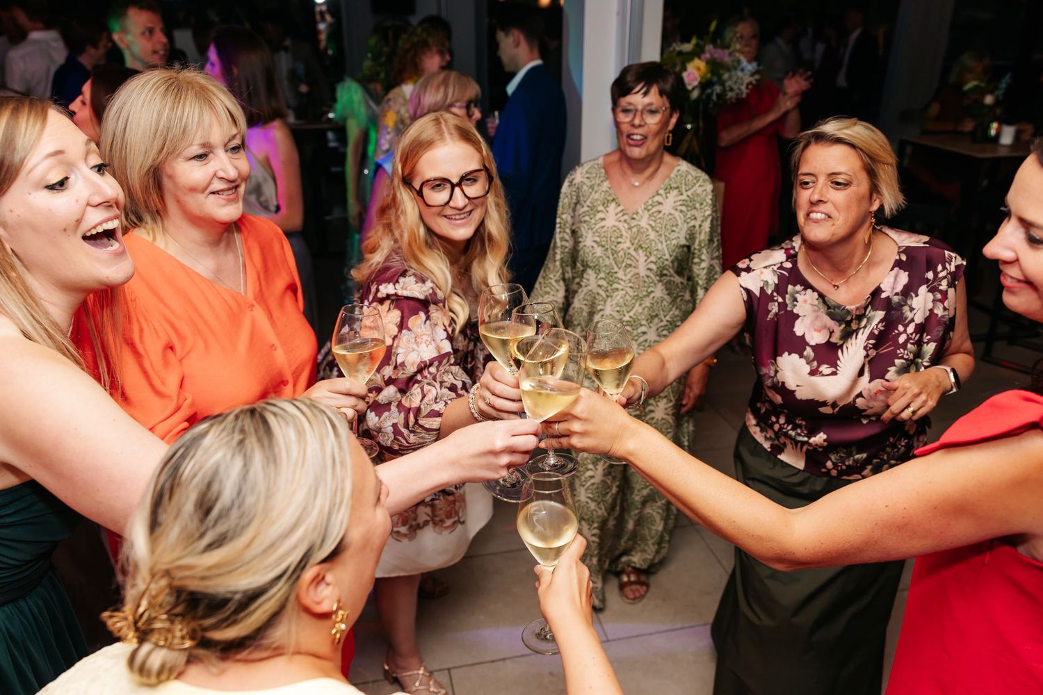 Group of women guests toasting with champagne glasses at lively wedding celebration.