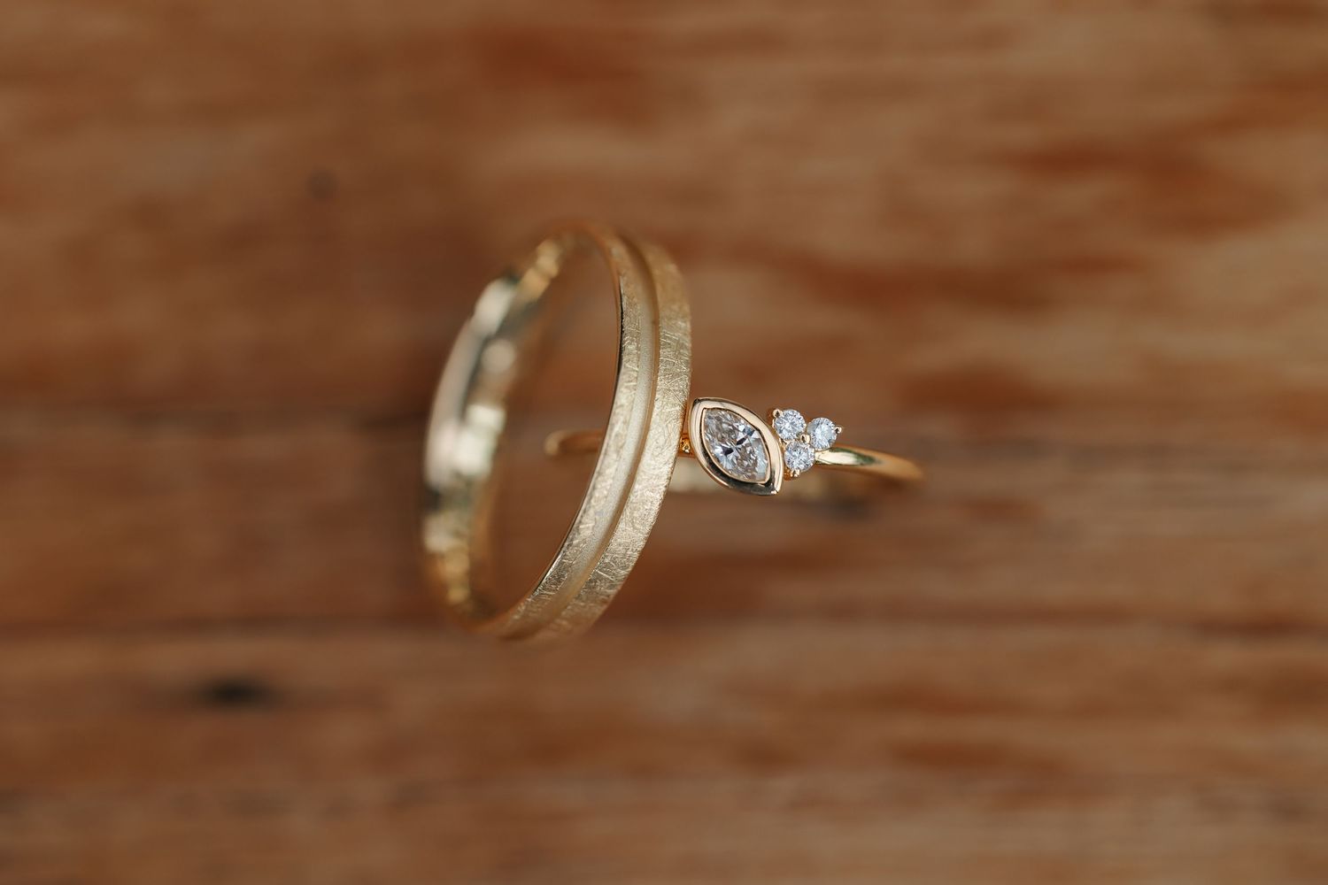 Gold wedding band and diamond marquise engagement ring displayed on rustic wood.