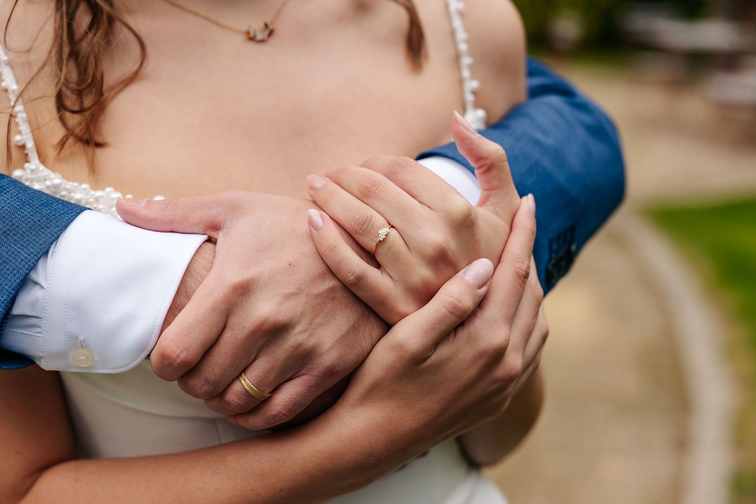Close-up of bride and groom's hands showing wedding rings in a loving embrace.