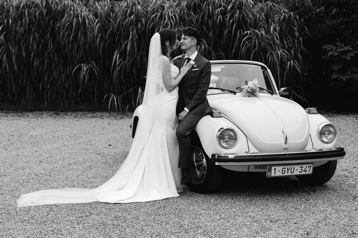 Black and white romantic photo of newlyweds kissing beside a vintage VW Beetle wedding car.