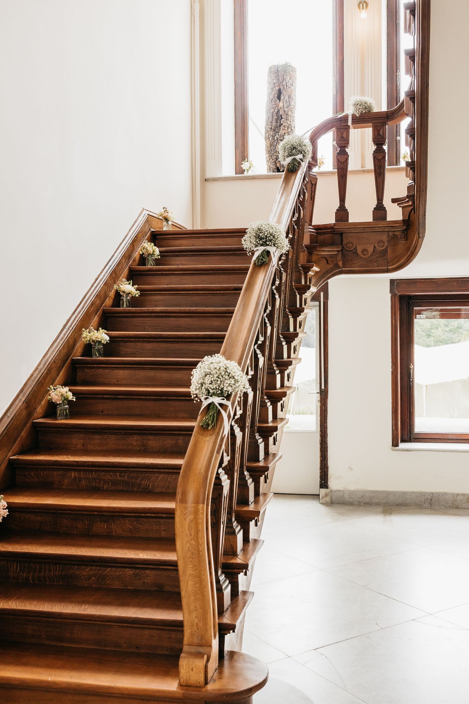 Elegant wooden staircase decorated with white floral bouquets for a wedding ceremony.