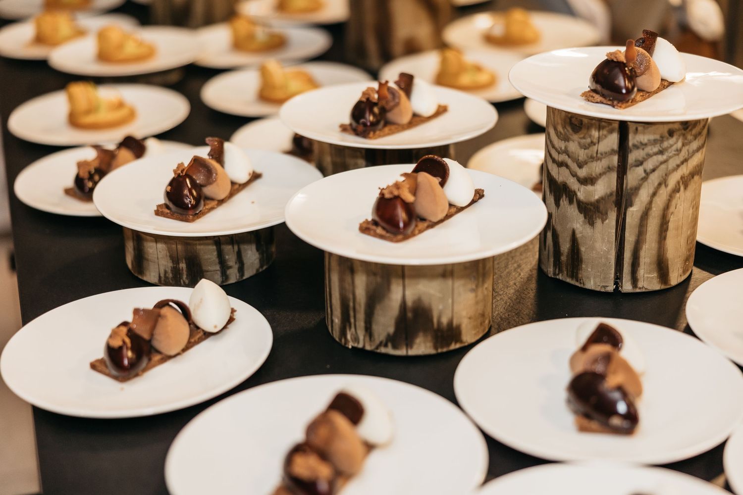 Gourmet chocolate wedding desserts elegantly plated on white dishes with wooden risers at reception.