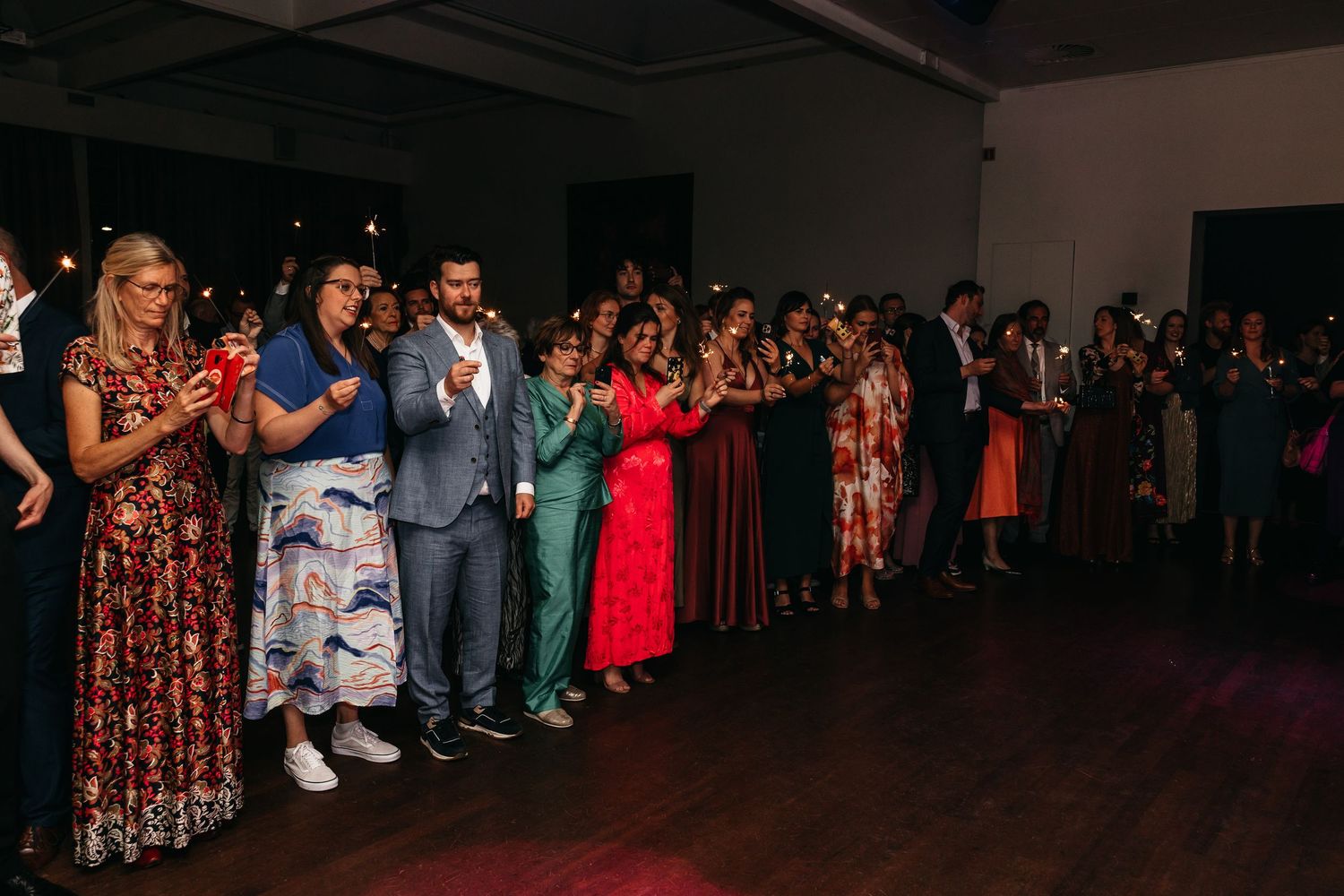 Wedding guests line the dance floor holding sparklers and applauding during reception celebration.