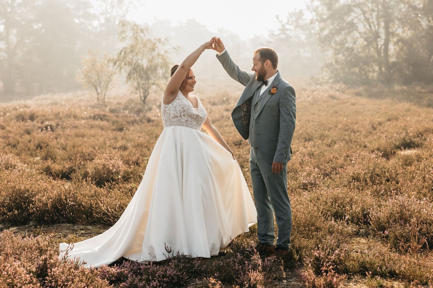 Elegant bride and groom twirling together in golden misty heather field during outdoor wedding photos.
