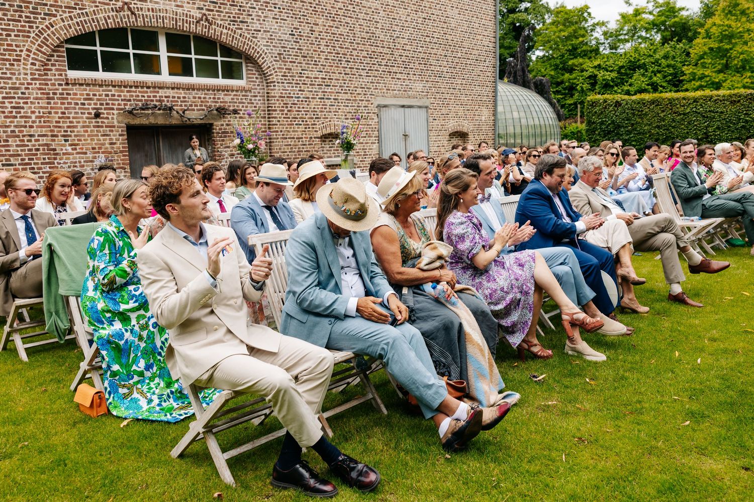 Elegant outdoor wedding ceremony with guests seated on white chairs in a sunny garden.