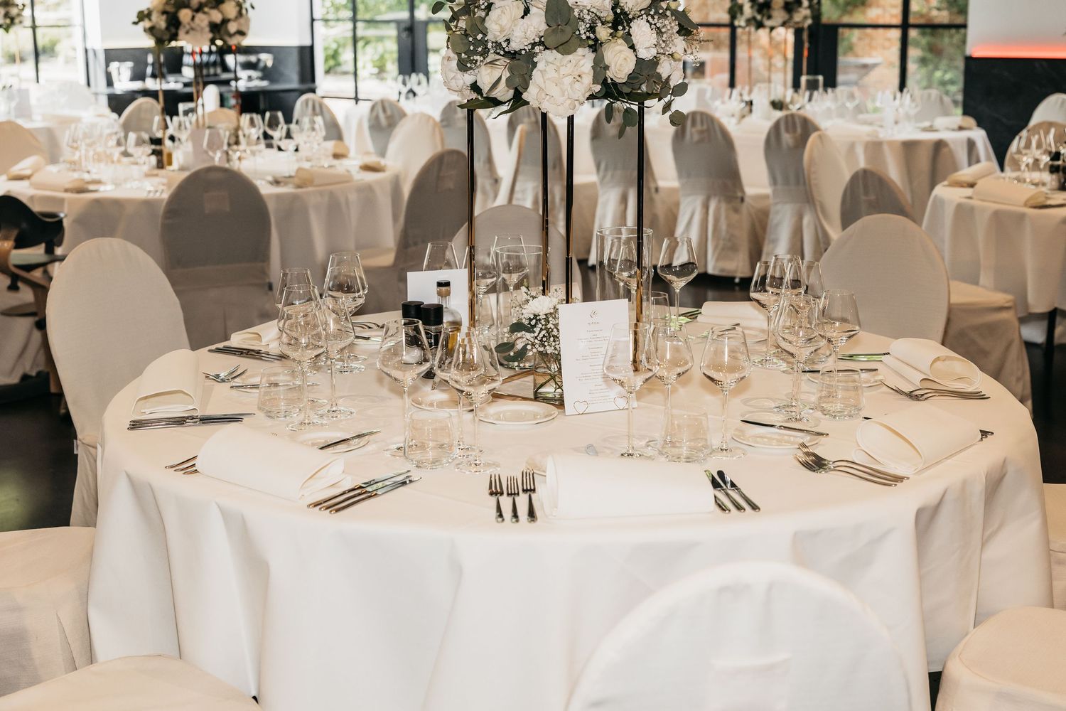 Elegantly set round wedding reception table with white linens, crystal glassware, and floral centerpieces.