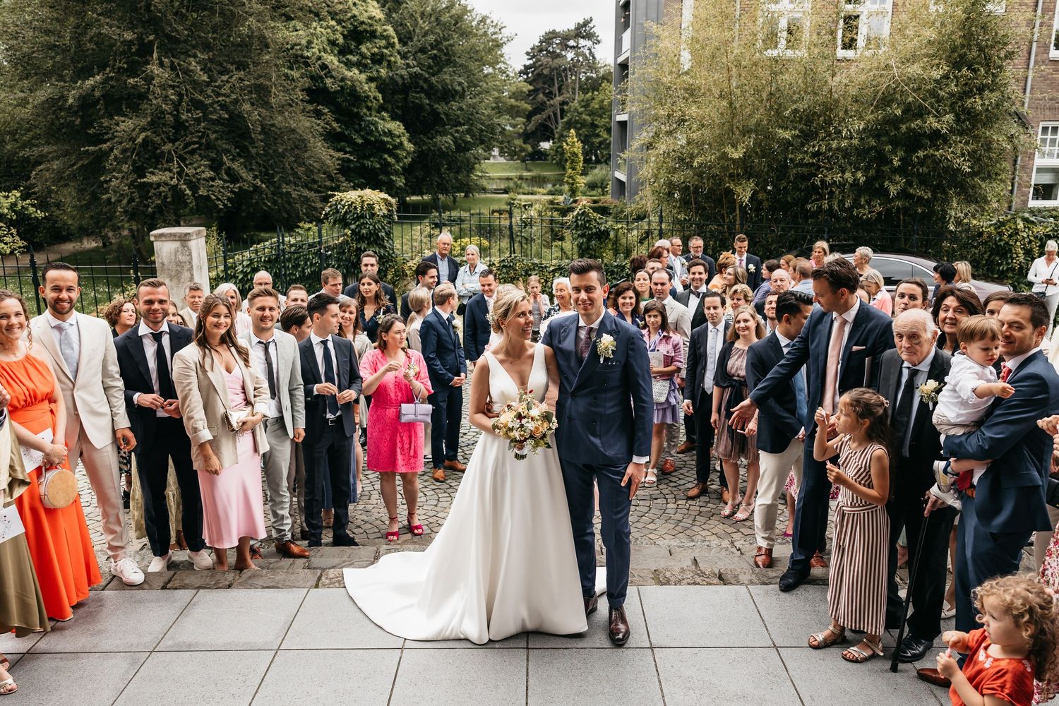 Newlyweds walk through crowd of celebrating wedding guests outside church.