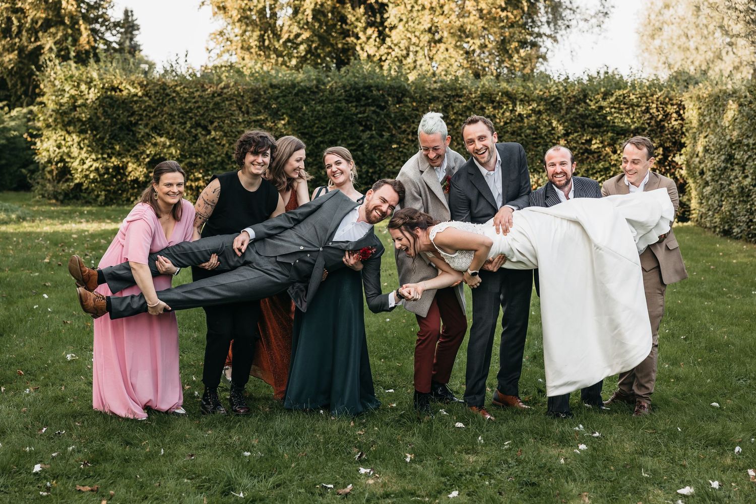 Wedding party lifting bride and groom horizontally in fun outdoor photo on green grass with autumn trees.