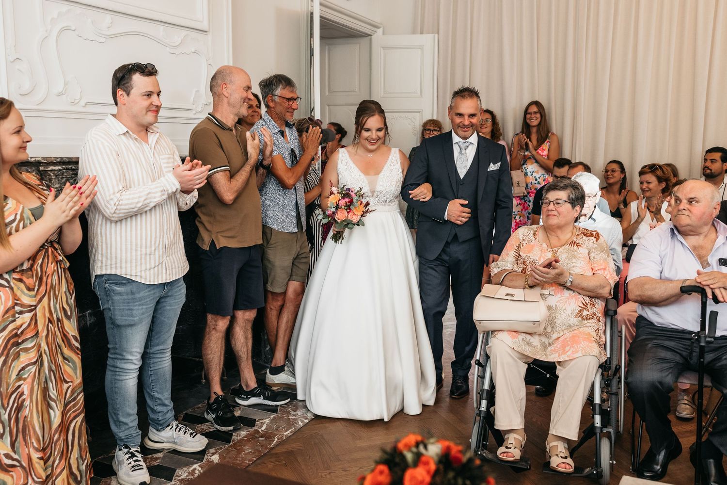 Bride walking down the aisle with older man while guests applaud during indoor wedding reception.