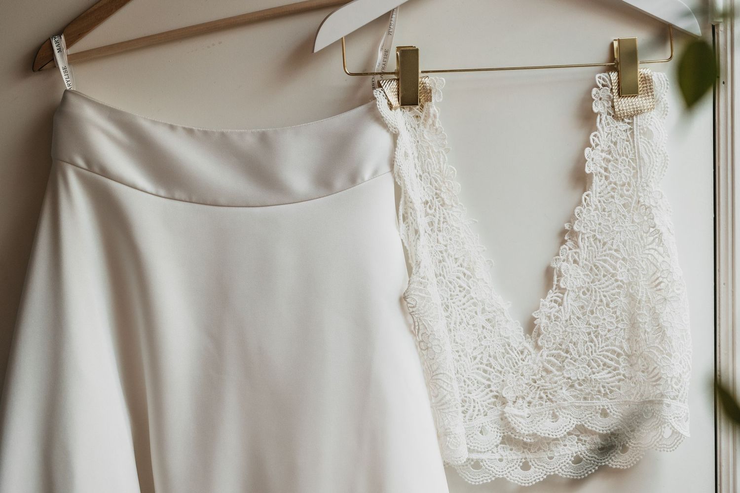Elegant white wedding dress with lace bodice hanging on a wooden hanger.
