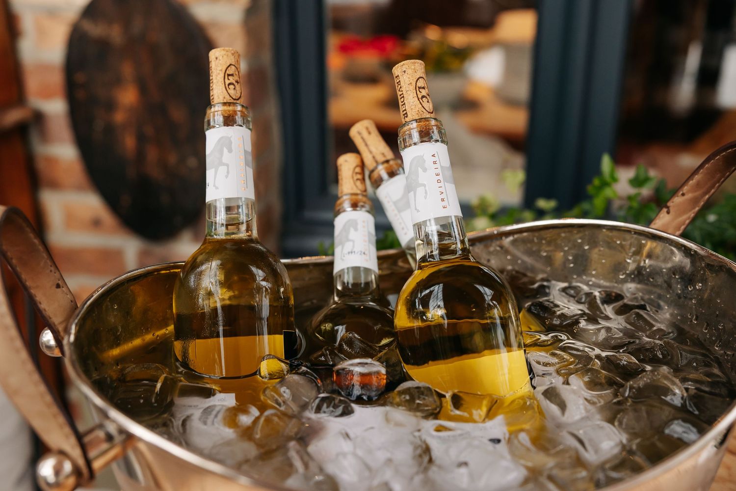 Three bottles of white wine chilling in an ice-filled metal bucket at a wedding reception.