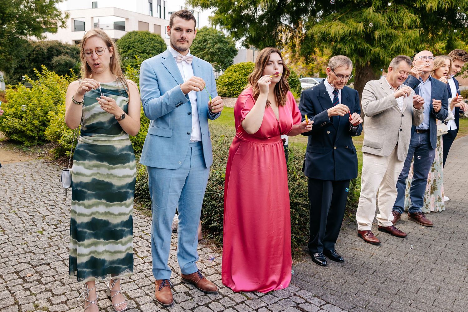 Wedding guests in formal attire blowing bubbles during an outdoor ceremony celebration.