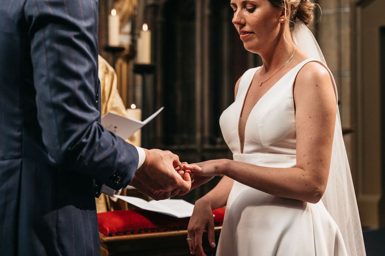Bride places wedding ring on groom's finger during church ceremony.