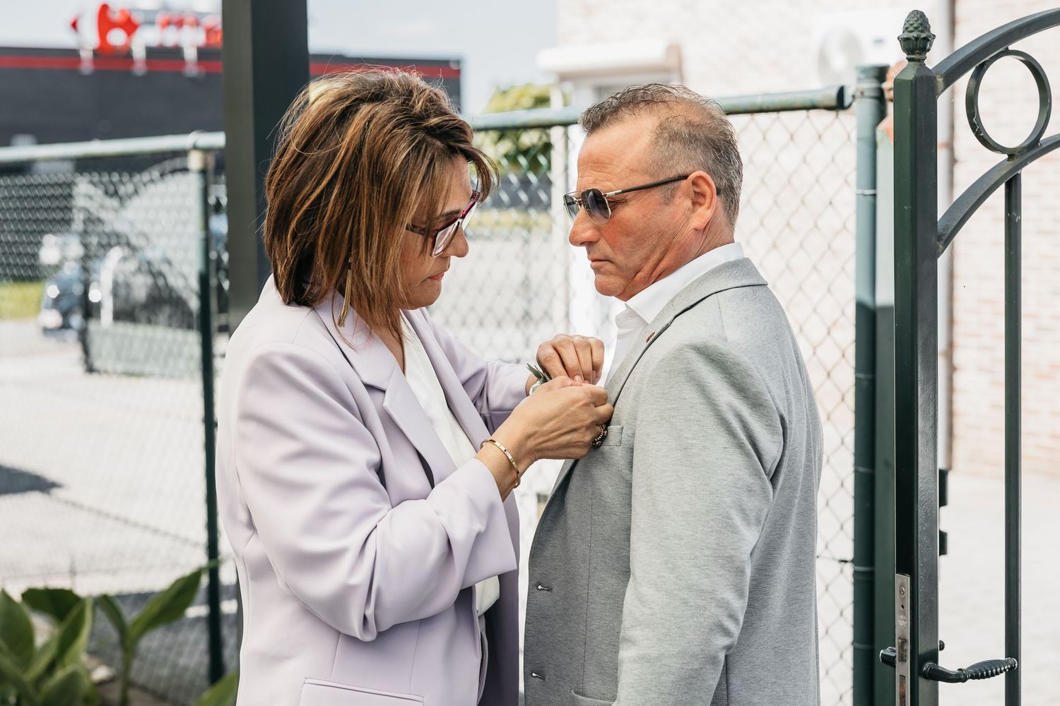 Woman pinning a boutonniere on a man in a grey suit at a wedding.