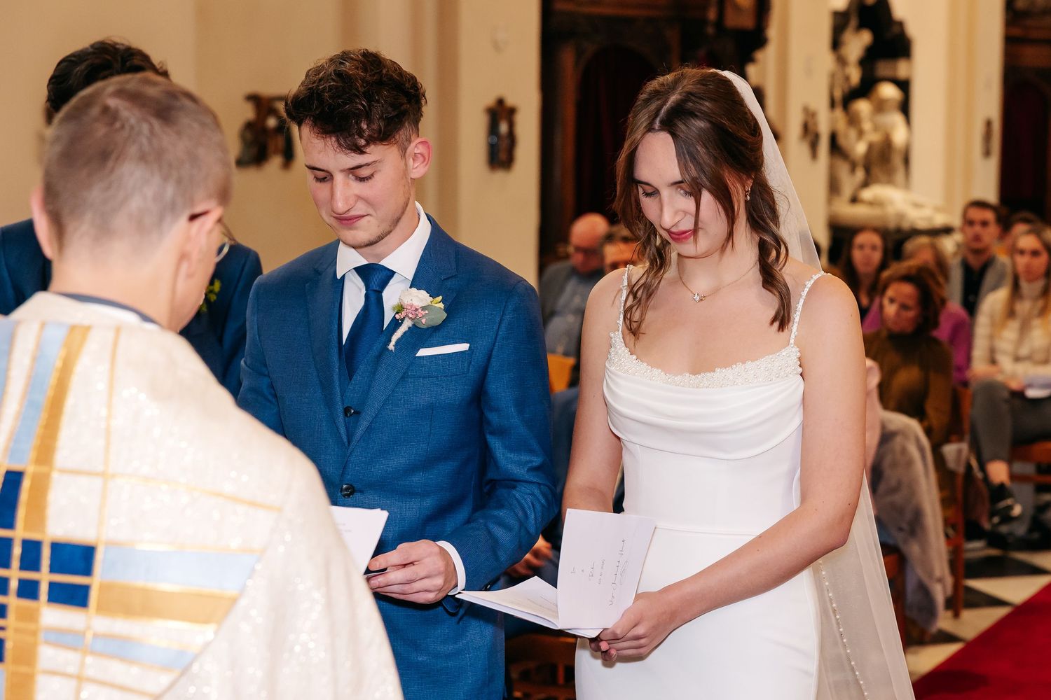 Bride and groom exchange vows with priest during intimate Catholic wedding ceremony.