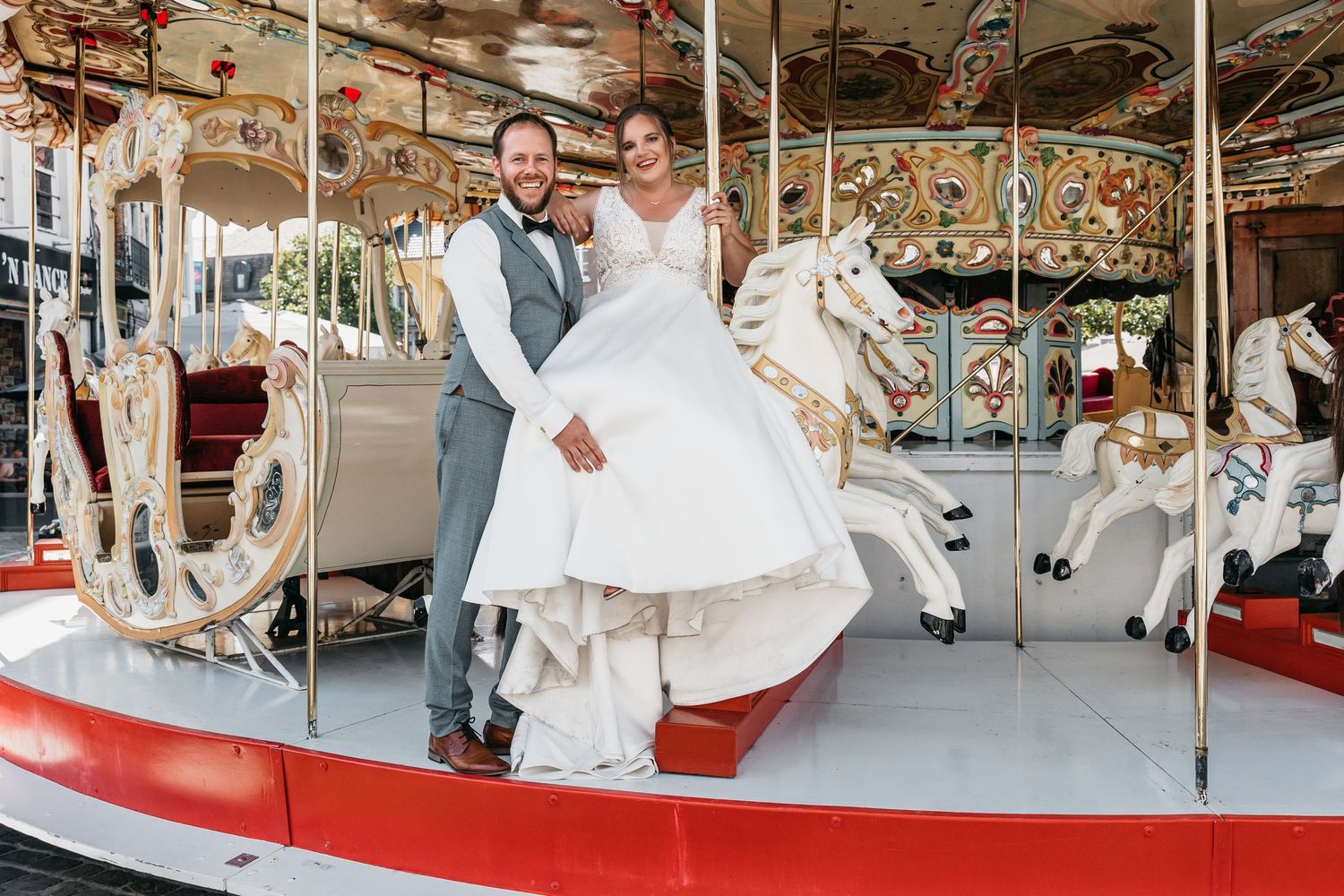 Bride and groom smiling together on a colorful carousel with white horses at their wedding celebration.