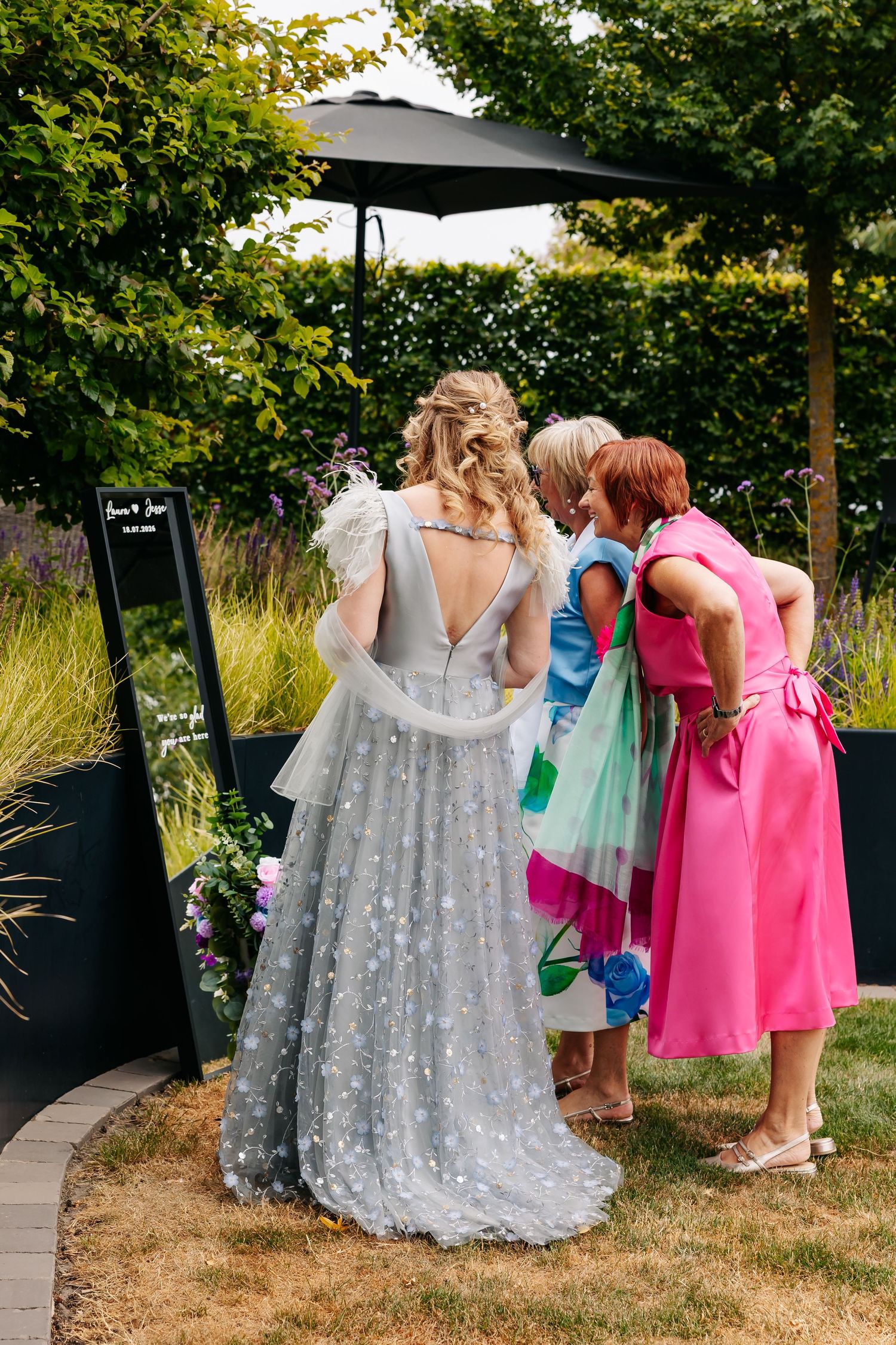 Bride in grey star-print gown viewed from behind with two guests at outdoor wedding.