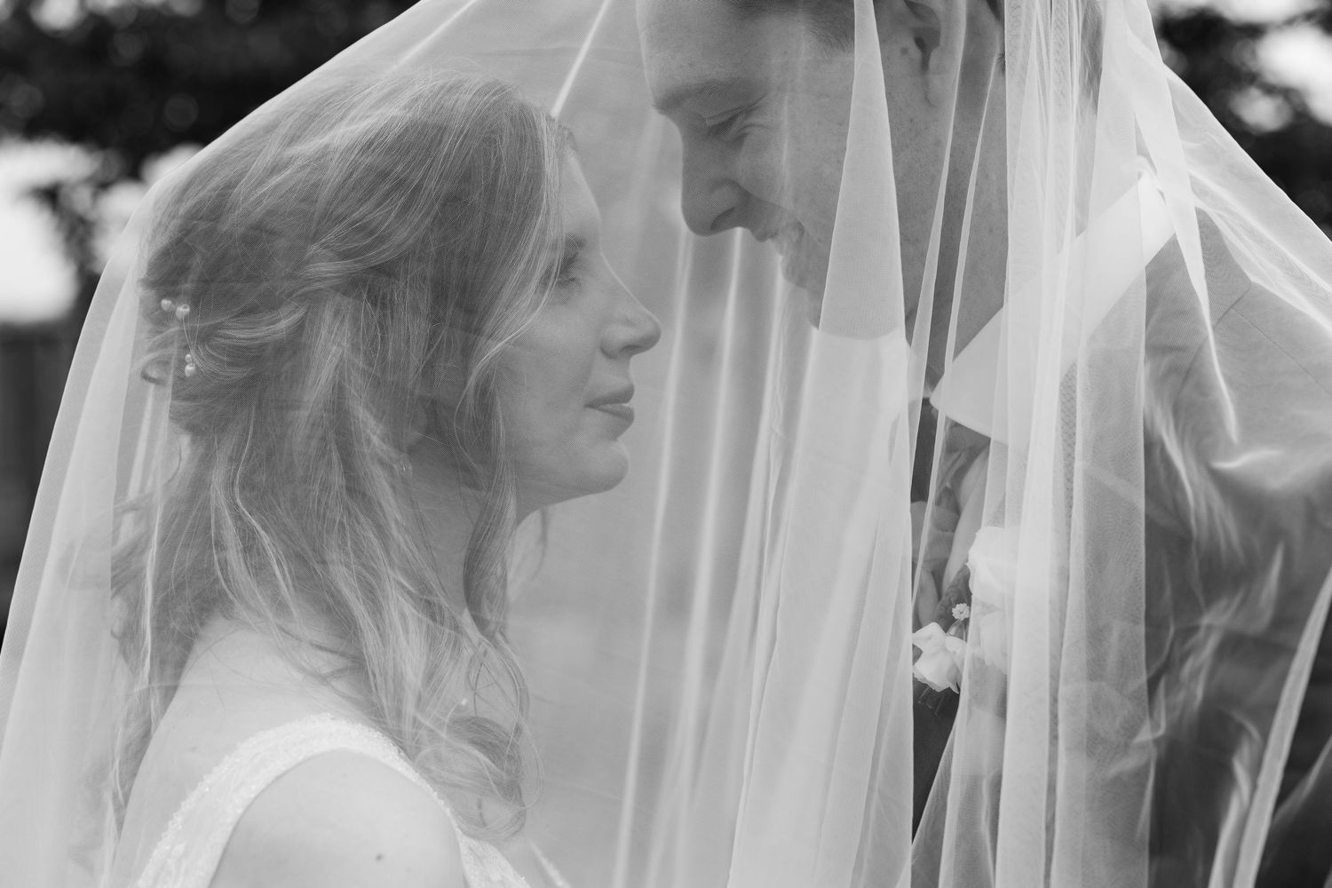Black and white romantic portrait of bride and groom sharing intimate moment under veil.