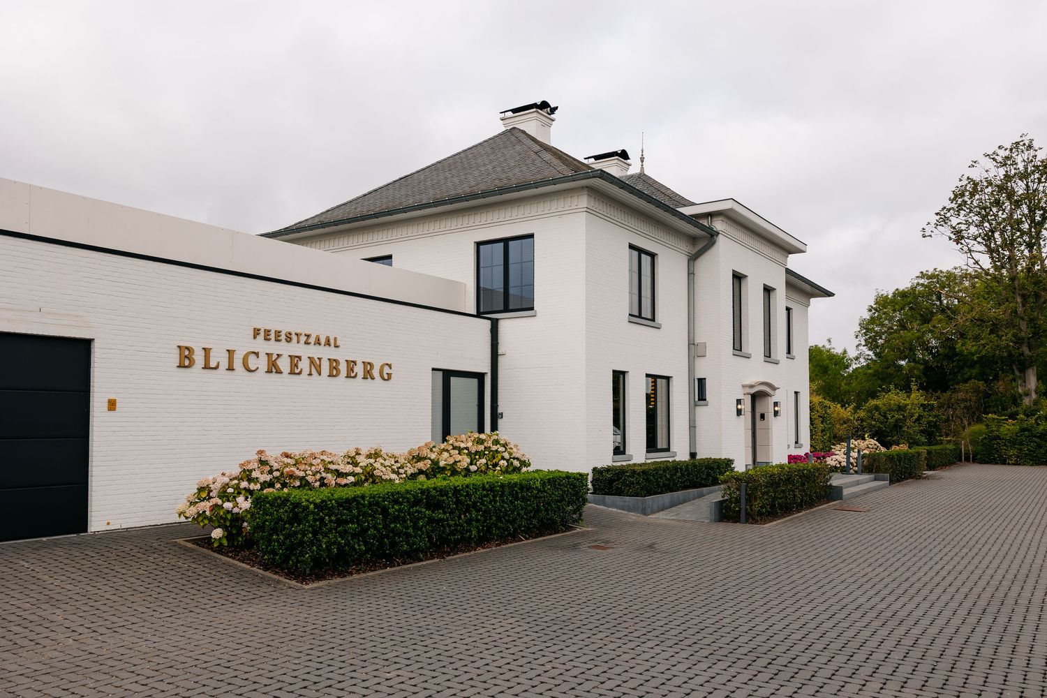 Elegant white wedding venue Blickenberg with manicured gardens and cobblestone driveway.