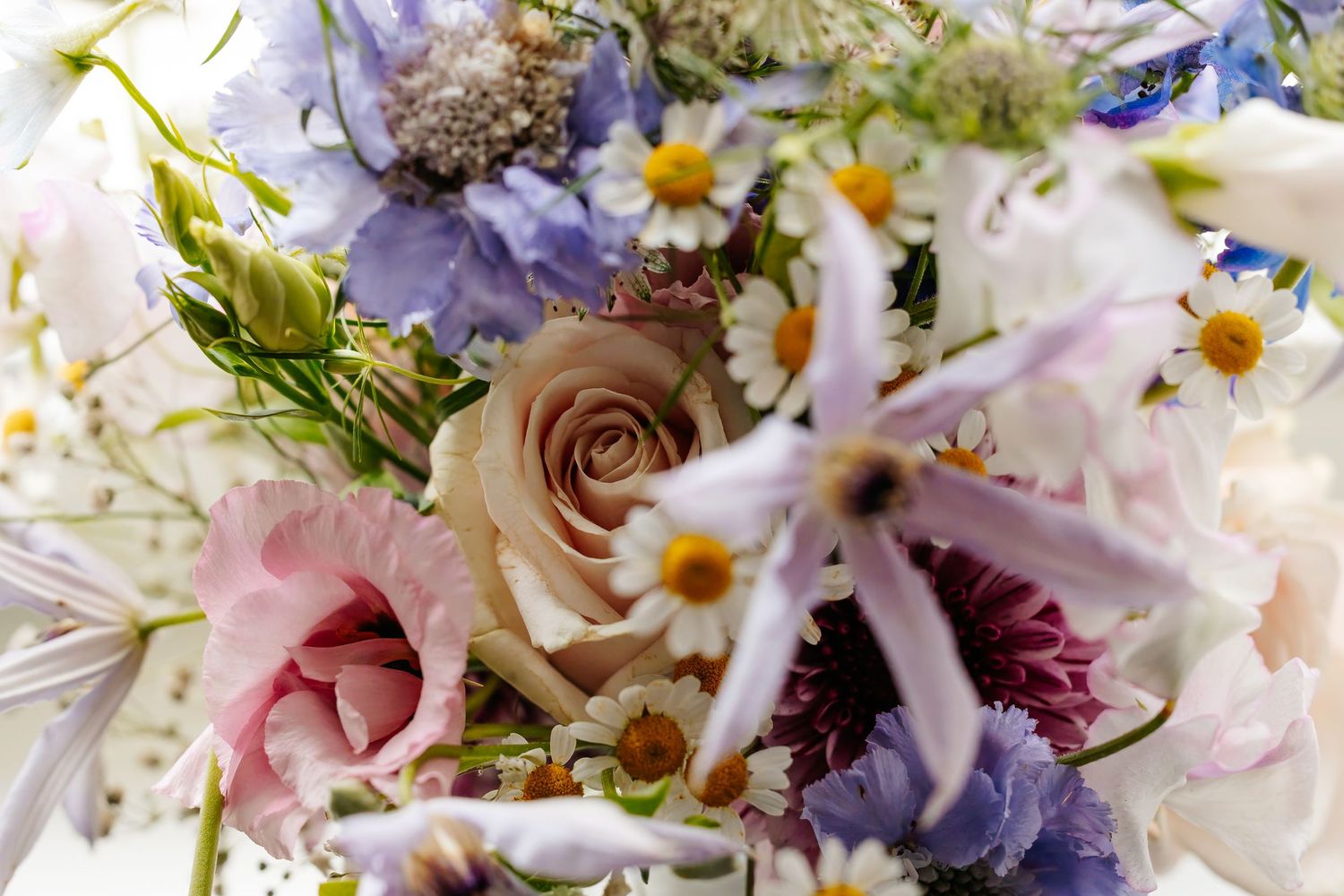 Beautiful bridal bouquet featuring soft pink roses, daisies, and wildflowers in pastel purple and blue hues.